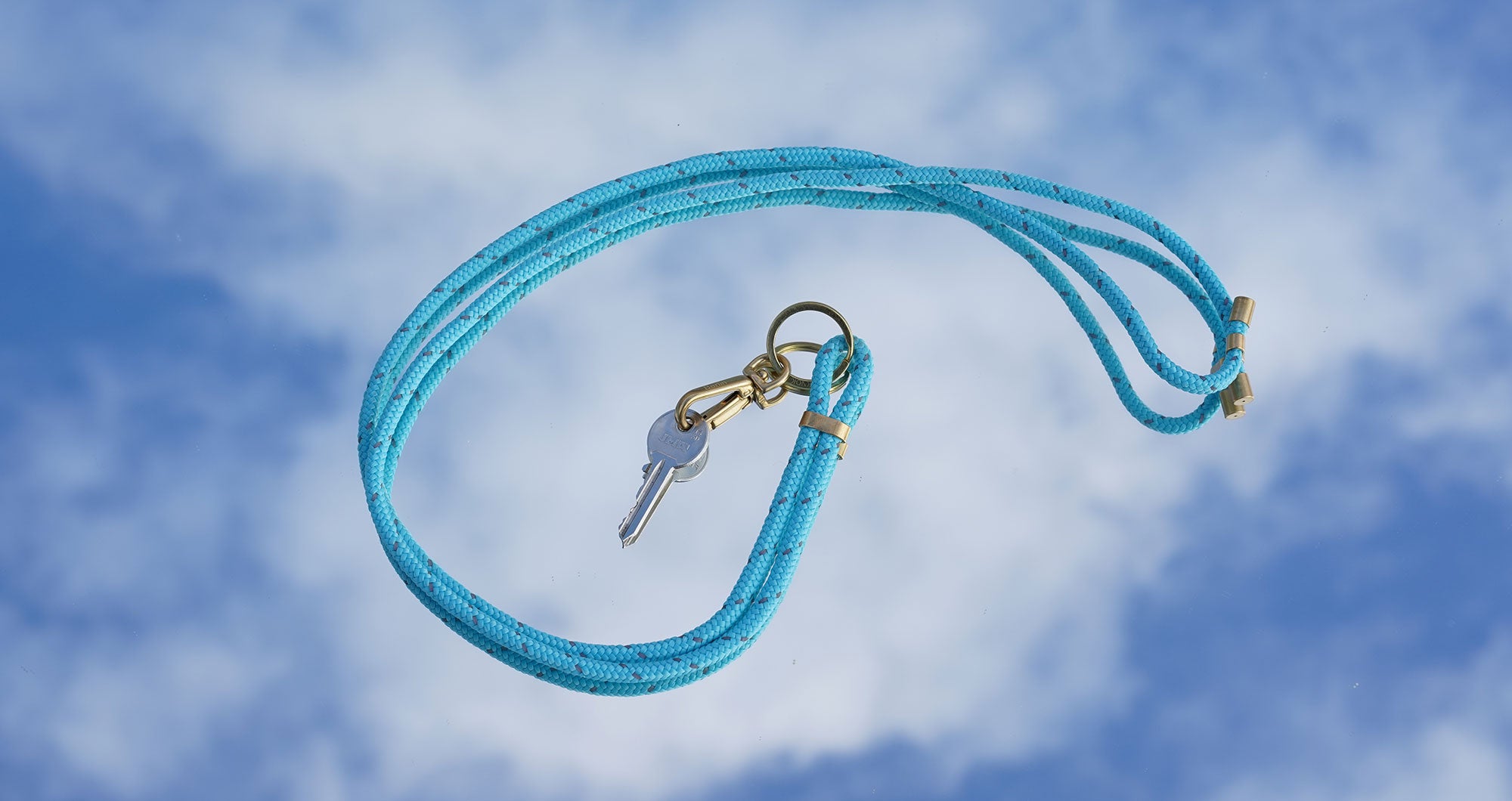 KNOK Key Holder Lanyard in Turquoise Reflect placed on a mirror reflecting blue sky and clouds